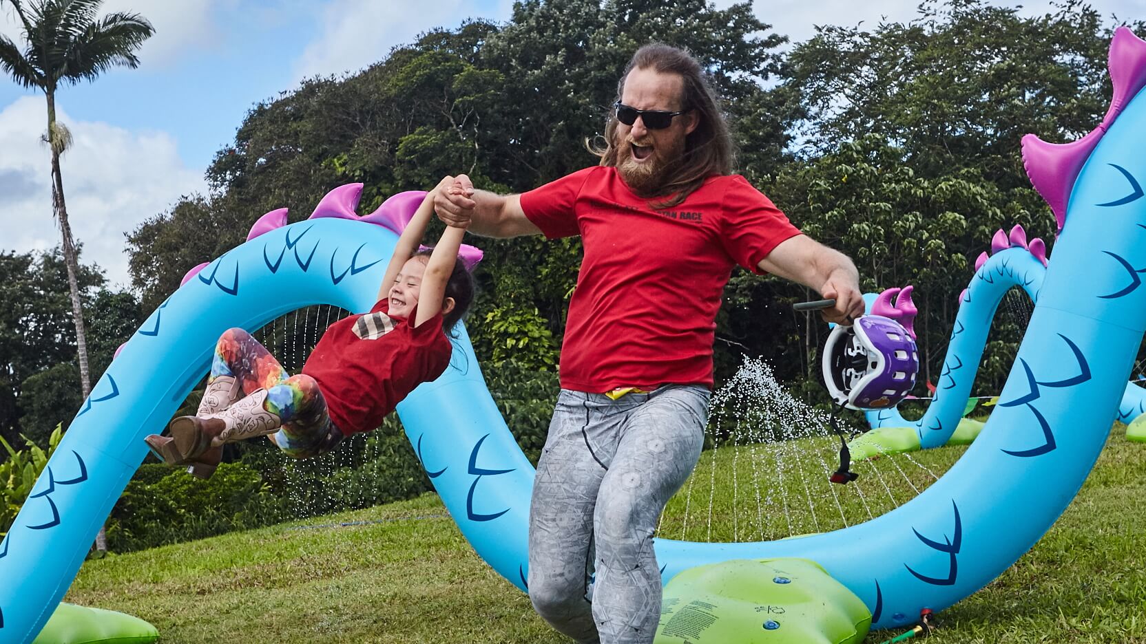 Father and child playing near inflatable sprinkler dragon.